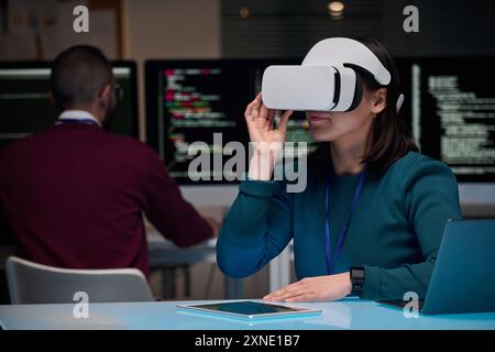 Portrait of young woman wearing VR headset in IT development office with code lines in background, copy space Stock Photo
