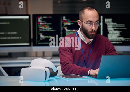 Portrait of bearded adult man wearing glasses and using laptop at desk in IT development office , copy space Stock Photo