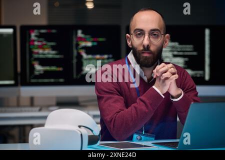 Portrait of bearded adult man wearing glasses and looking at camera while sitting at desk in IT development office , copy space Stock Photo