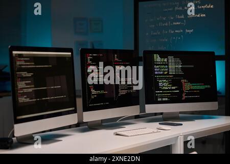 Background image of three computer monitors with code lines on table in IT development office, copy space Stock Photo