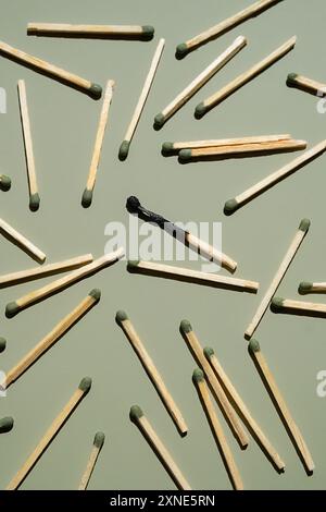 Scattered matches with one burnt matchstick on light green background. Stock Photo
