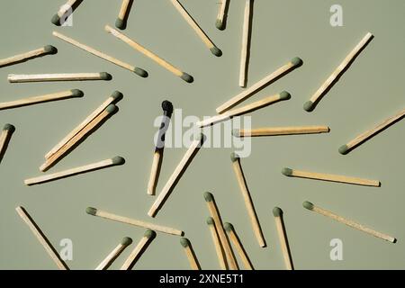 Scattered matches with one burnt matchstick on light green background. Stock Photo