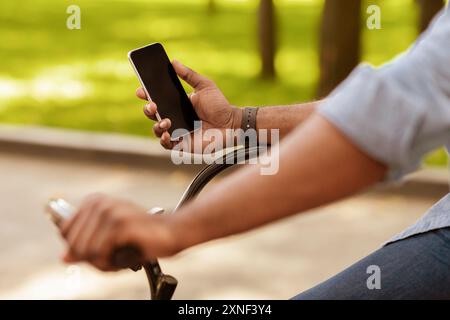 Afro man riding bike and using smartphone with black screen Stock Photo