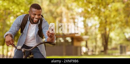 Happy Black Man Riding Bicycle Outdoors And Using Smartphone Stock Photo