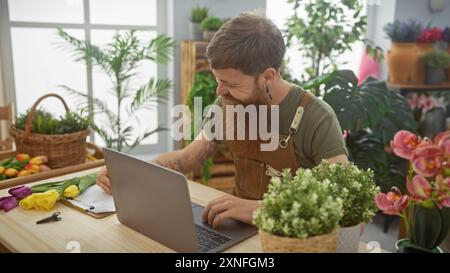 Handsome redhead man with beard taking notes on clipboard at laptop in a lush flower shop Stock Photo