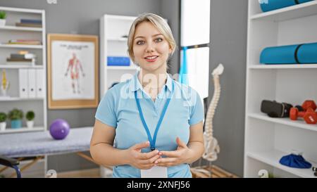 A professional young woman stands confidently in a rehabilitation clinic, surrounded by anatomical charts and physiotherapy equipment. Stock Photo