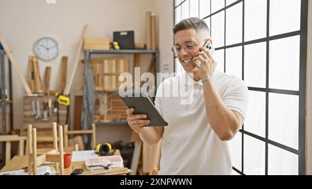 Smiling hispanic man using tablet and phone in a carpentry workshop Stock Photo