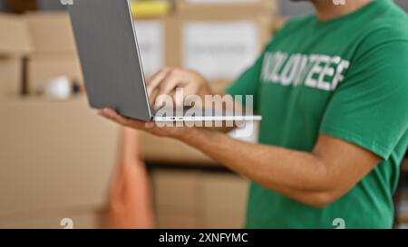Hispanic man using laptop at warehouse workplace, reflecting logistics, technology, and business aspects. Stock Photo