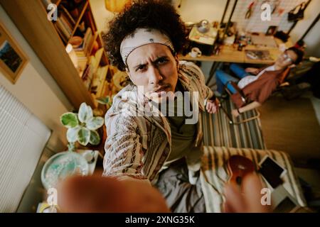 Curly-haired man with black and white bandana putting security camera while standing on bed in dorm room Stock Photo