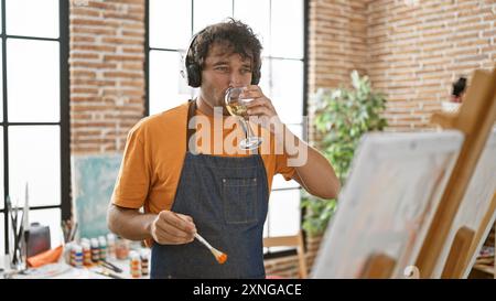 Handsome hispanic man sipping wine and painting in a bright studio Stock Photo