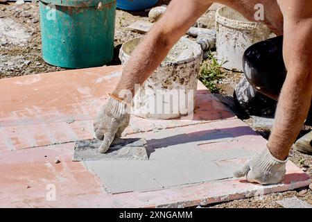 Construction worker house painter uses steel trowel to apply tile adhesive to trim panel. Stock Photo