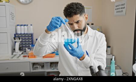 Handsome bearded man conducts experiments with a blue liquid in a medical laboratory setting, wearing gloves and a lab coat. Stock Photo