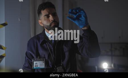 A focused hispanic detective examines evidence at an indoor crime scene with meticulous care and professionalism. Stock Photo