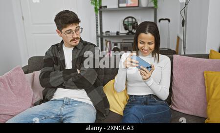 A woman plays on her phone while a bored man watches in a cozy living room setting. Stock Photo