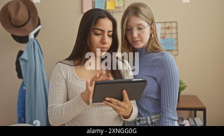 Two women using a tablet together in a cozy living room setting, evoking a sense of friendship and technology at home. Stock Photo