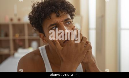 Young hispanic man in a spa thinking deeply while sitting indoors in a serene wellness center Stock Photo