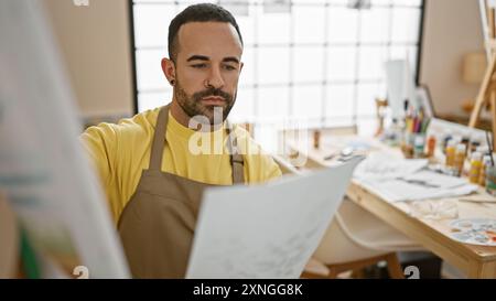 A focused man holding paper in an art studio examines his work with a contemplative expression. Stock Photo
