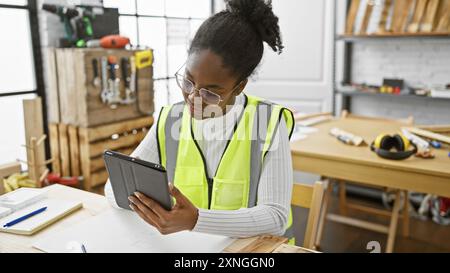 A focused african american woman reading a tablet in a well-equipped carpentry workshop Stock Photo
