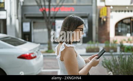 Beautiful hispanic woman with glasses walking confidently on tokyo streets while engrossed in her phone, typing a serious business text Stock Photo