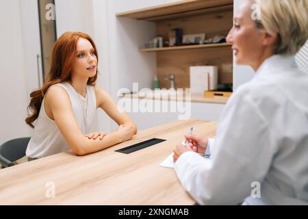 Rear view of middle-aged female doctor giving psychological support to young woman patient, talking, speaking. Sad lady visiting practitioner for Stock Photo