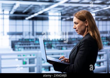 Admin implementing backup solutions in in data center service business to protect against equipment data loss using laptop. Expert resolving technical malfunctions affecting rackmounts using notebook Stock Photo