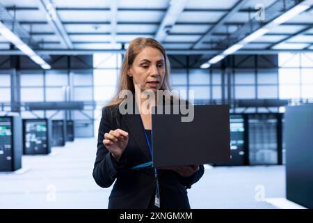System administrator in server room using laptop to implement and maintain security measures, protecting systems from unauthorized access. Data center IT expert doing hardware upgrades using notebook Stock Photo
