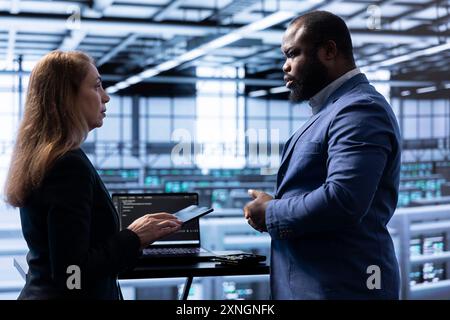 Team of programmers in data center establishment doing yearly infrastructure inspection. Teamworking colleagues in server farm monitoring supercomputers equipment with laptop Stock Photo