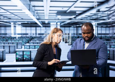 Team of programmers in data center checking rigs and hardware, doing checkup. Teamworking colleagues planning and executing high tech server hub facility migrations and upgrades Stock Photo