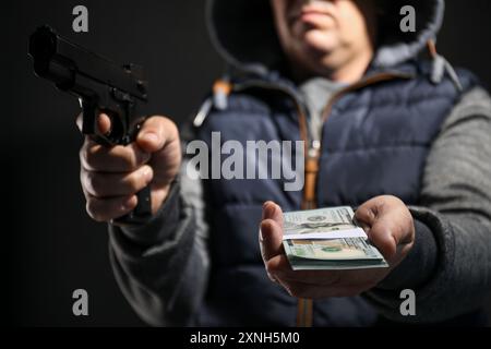 Dangerous criminal with gun holding money on black background, selective focus. Armed robbery Stock Photo