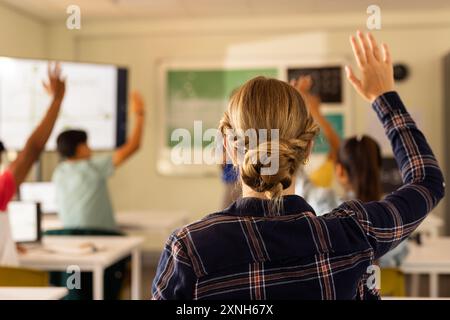 In high school, students raising hands in classroom, actively participating in lesson Stock Photo
