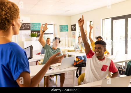 In high school, students raising hands and engaging with teacher in classroom Stock Photo