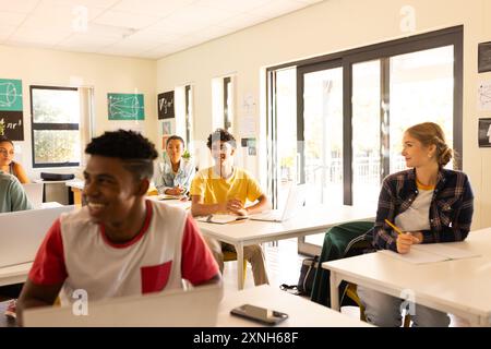 In high school, teenagers sitting at desks with laptops, smiling and engaging in class Stock Photo