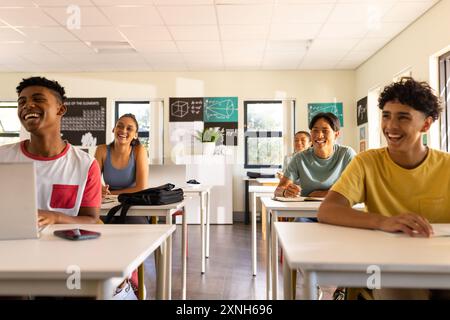 Teenagers in high school classroom, sitting at desks and smiling, enjoying lesson Stock Photo