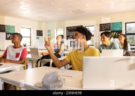 In high school, teenagers using laptops and raising hands in classroom discussion Stock Photo