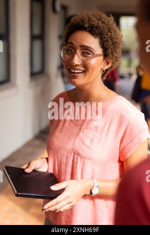 Smiling teenager holding notebook, standing in high school hallway, wearing glasses Stock Photo