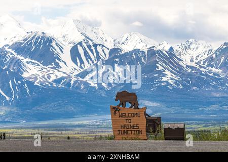 Spring time view Haines Junction in northern Canadian area with welcome sign featuring a bear and massive, huge snow capped mountains background Stock Photo