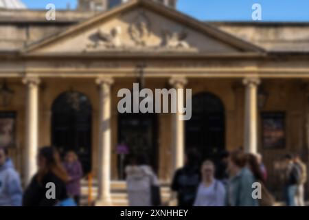 An out-of-focus image shows a group of people walking past a large stone building with a columned portico, perhaps a Roman bath. Stock Photo