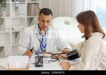 Handsome doctor measuring patient's blood pressure at table in clinic Stock Photo