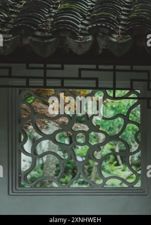 A white frame with an intricate design outlines a view of lush greenery in a Chinese garden. Stock Photo