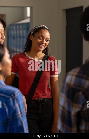 Smiling teenager with backpack talking with friends in high school hallway Stock Photo