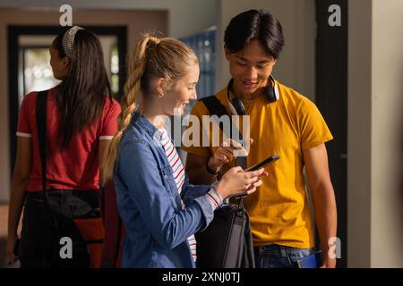 Teenagers in high school hallway looking at smartphone and smiling together Stock Photo