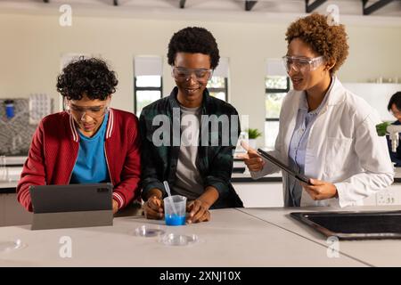 Conducting science experiment with tablet and beaker, teenagers in high school classroom Stock Photo