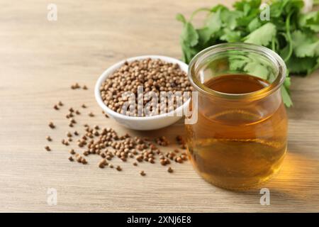 Dried coriander seeds in bowl, oil and green leaves on wooden table Stock Photo