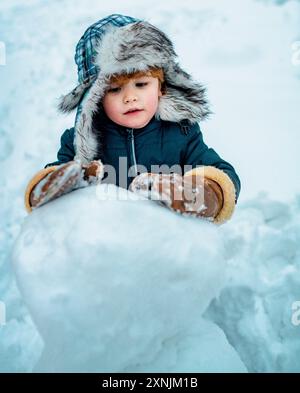 Excited kid winter portrait. Kids emotion. Winter clothes for kids. Joyful kid Having Fun with snowman in Winter Park. Stock Photo