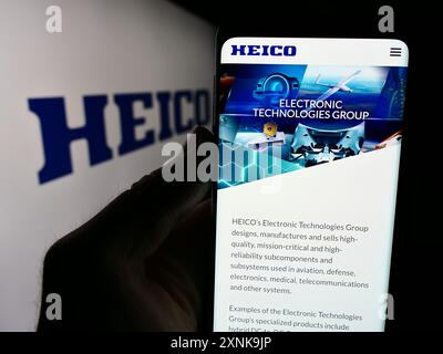 Person holding cellphone with webpage of US aerospace company HEICO Corporation in front of business logo. Focus on center of phone display. Stock Photo