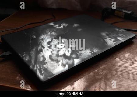 Flower-shaped shadows from tulle fall on laptop. Floral pattern. Stock Photo