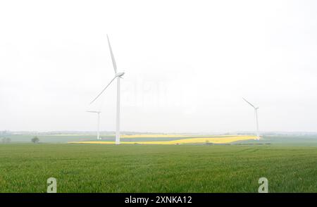 An electricity generating windmills on the yellow and green field against cloudy blue sky  in England Stock Photo