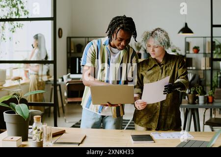 Young Caucasian woman with disability and her Black male colleague working together on report in eco-friendly office Stock Photo