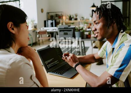 Gen Z African American male and Asian female programmers working on modern software discussing coding issues Stock Photo