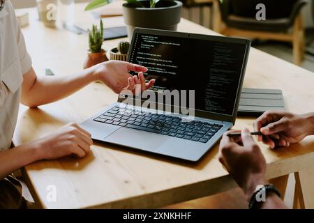 Unrecognizable biracial male and female programmers sitting at wooden desk and working together on code using laptop Stock Photo
